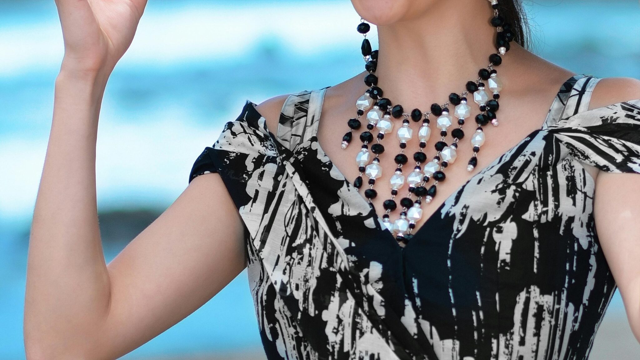 Close-up of a woman's chic outfit with a striking necklace by the seaside.