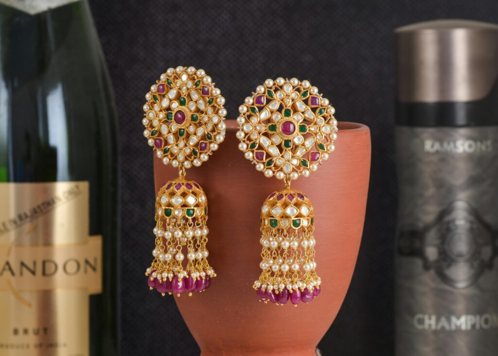 Exquisite gold earrings adorned with pearls and gemstones elegantly displayed on a clay pot.