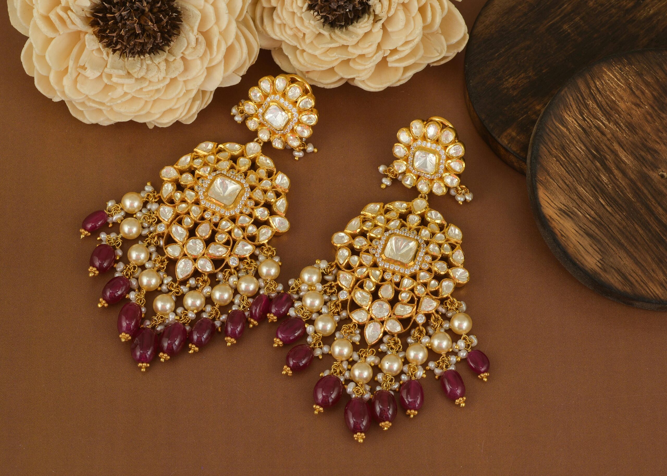Luxury beaded pearl and ruby earrings arranged on a brown surface with floral decor.